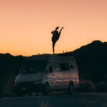 silhouette of a person doing a standing split on top a vans roof